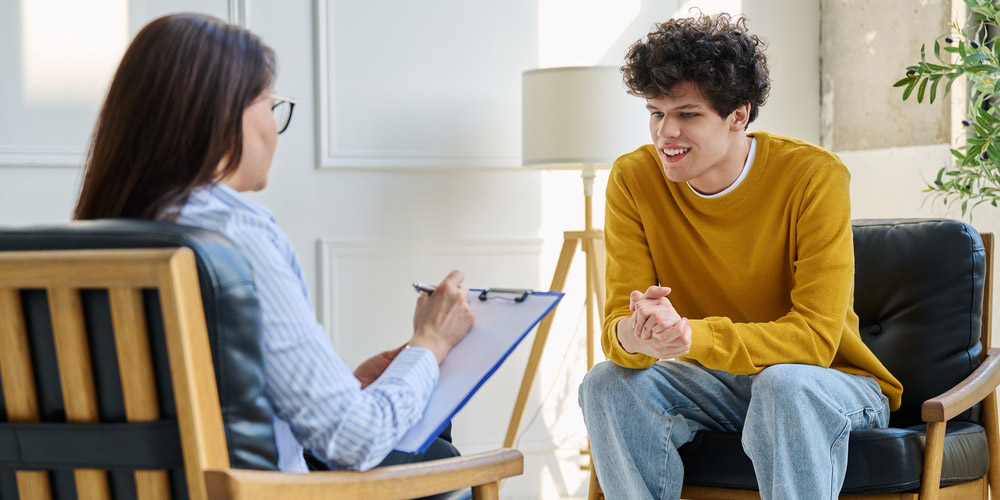 Happy,Teenage,Boy,Smiling,During,Successful,Consultation,With,Female,Psychologist